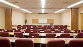 A conference room with rows of tables and chairs, a whiteboard, and an exit door.