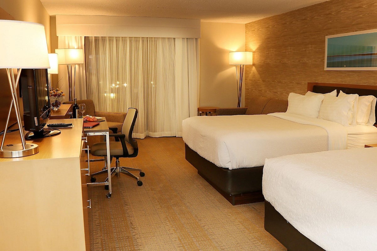 Ein Hotelzimmer mit zwei Betten, einem Schreibtisch mit Stuhl, einer Lampe und einem Bild an der Wand.