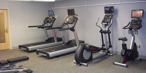 A gym with treadmills, an elliptical, and a bench. - enVision Hotel & Conference Center Mansfield-Foxboro (Mansfield)