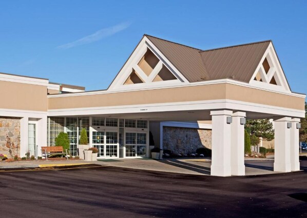 A modern building with a large entrance, stone facade, and a covered parking area. - enVision Hotel & Conference Center Mansfield-Foxboro (Mansfield)