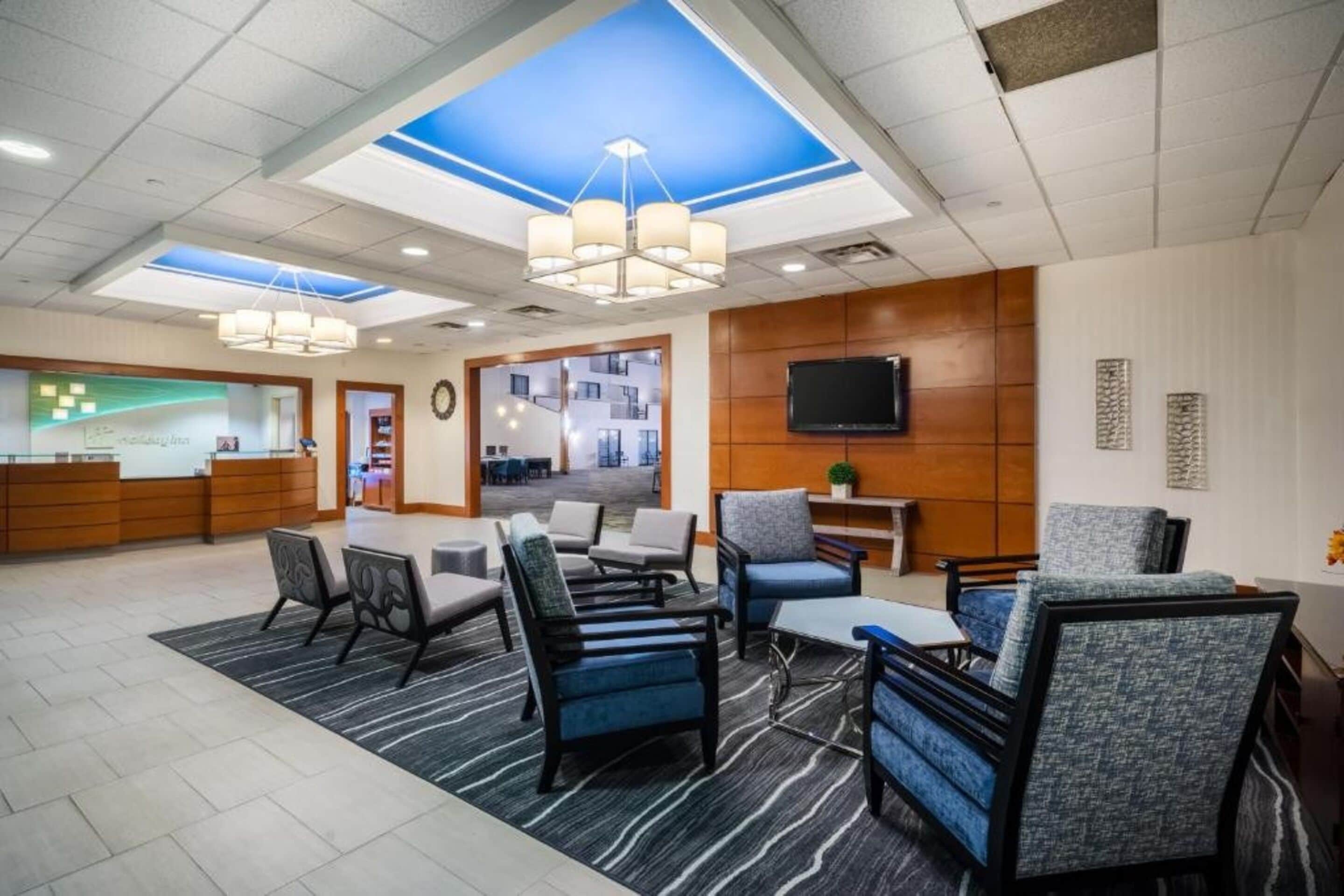 A modern lobby with a reception desk, seating area, and a large TV screen.