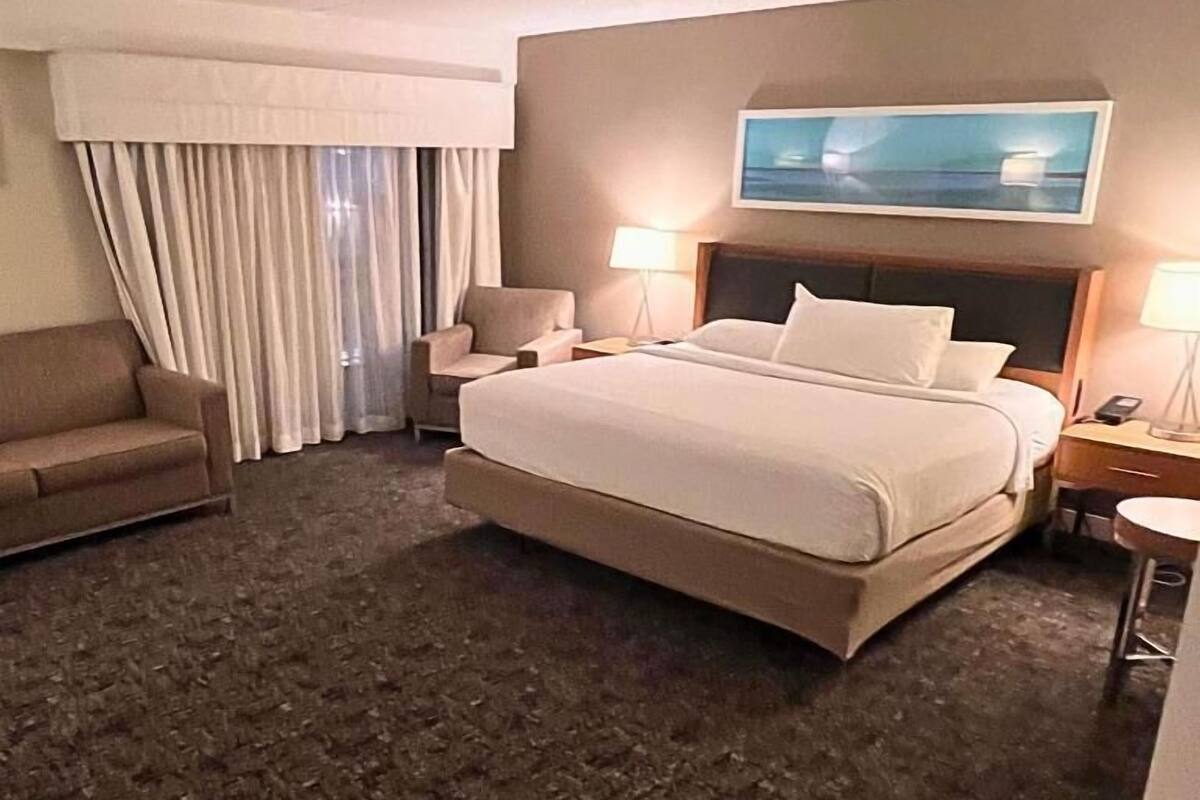 Ein Hotelzimmer mit einem großen Bett, zwei Nachttischen, einem Sessel und einem Bild an der Wand.