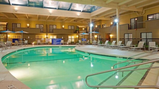 An indoor swimming pool with lounge chairs and umbrellas, surrounded by a multi-level building with balconies. - enVision Hotel & Conference Center Mansfield-Foxboro (Mansfield)