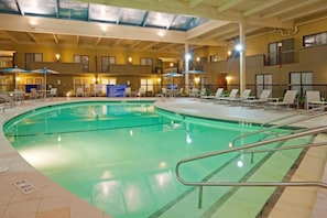 An indoor swimming pool with lounge chairs and umbrellas, surrounded by a multi-level building with balconies. - enVision Hotel & Conference Center Mansfield-Foxboro (Mansfield)