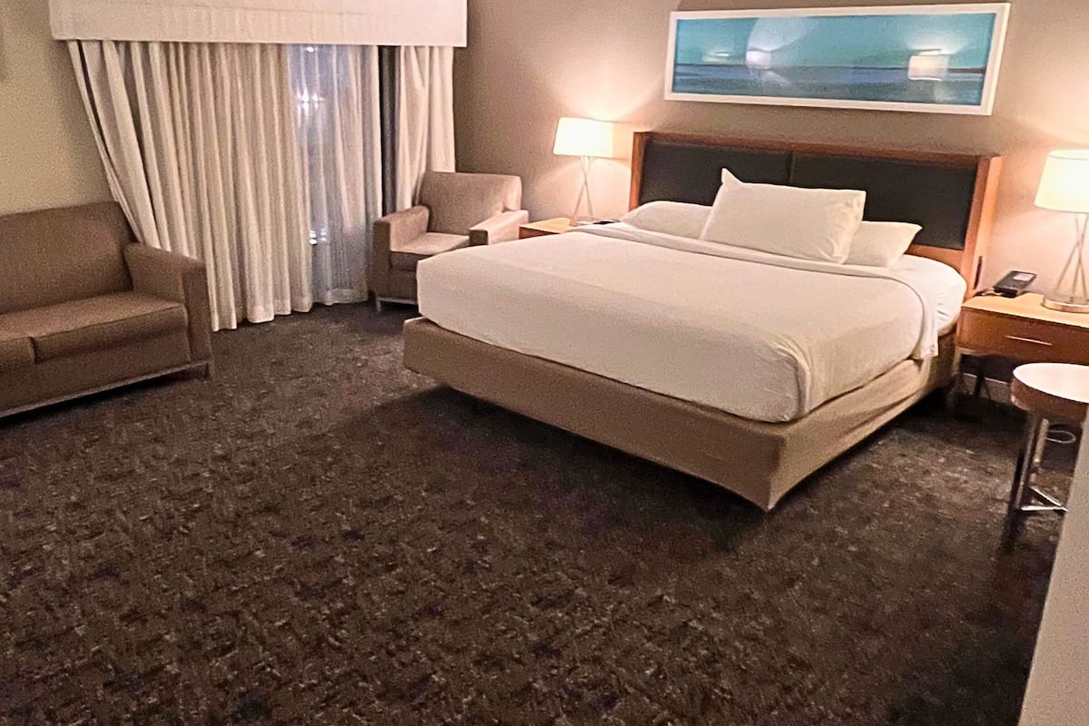 Ein Hotelzimmer mit einem großen Bett, einem Sessel, einem Schreibtisch und einem Bild an der Wand.