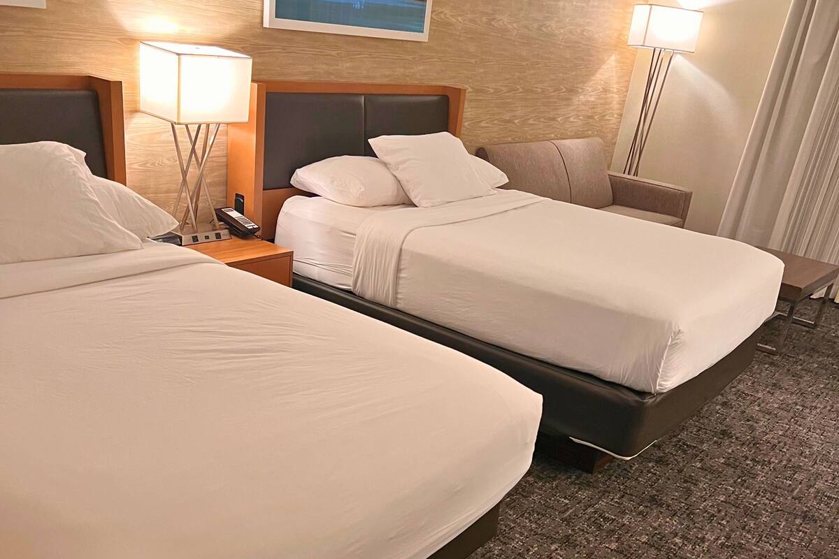 Ein Hotelzimmer mit zwei Betten, einem Nachttisch mit Lampe und einem an der Wand montierten Telefon.