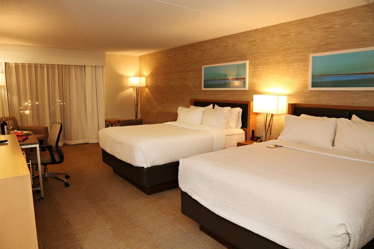 Ein Hotelzimmer mit zwei Betten, einem Schreibtisch, einem Stuhl, einer Lampe und einem Bild an der Wand.