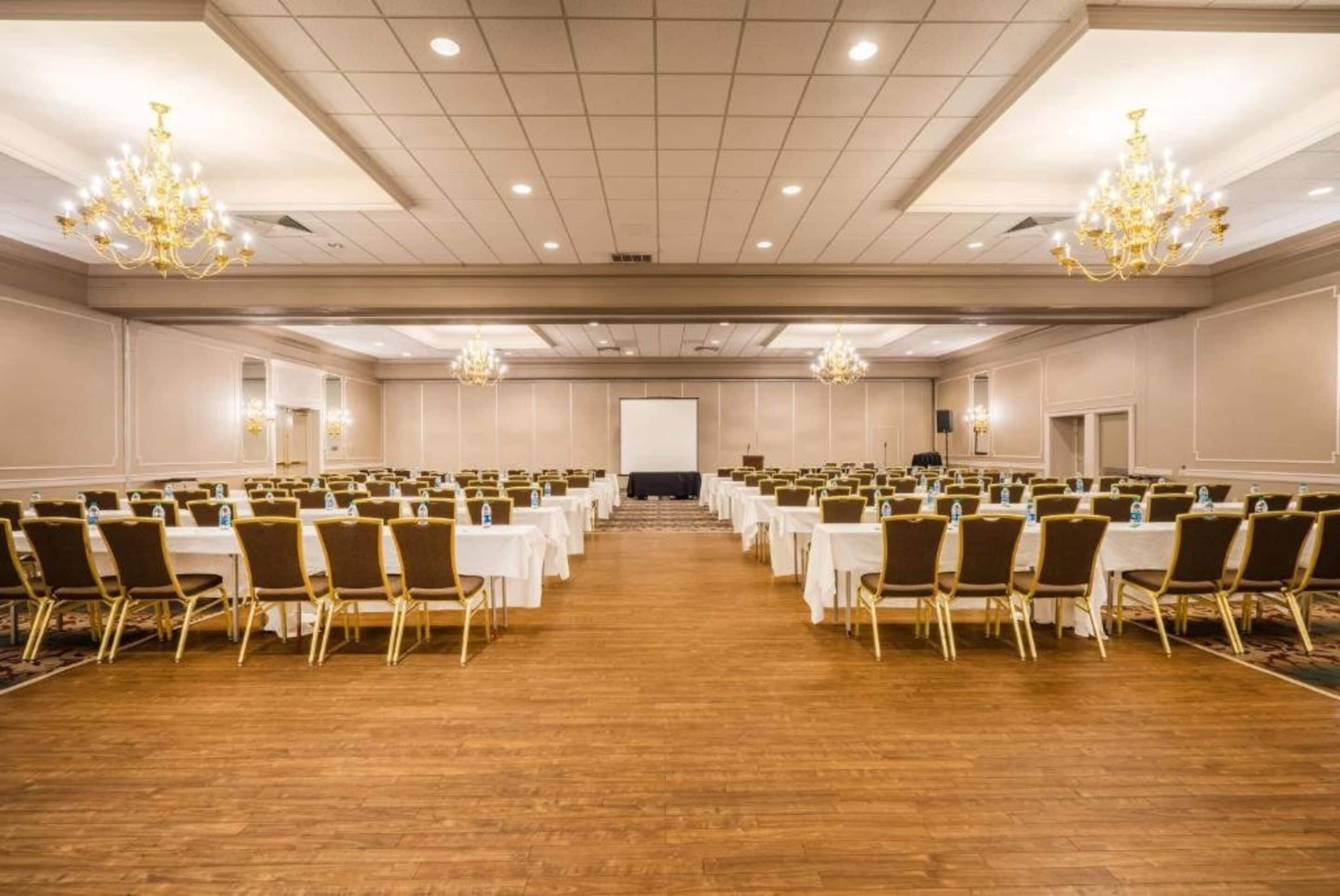 Una sala conferenze con file di tavoli e sedie, un palco e lampadari.