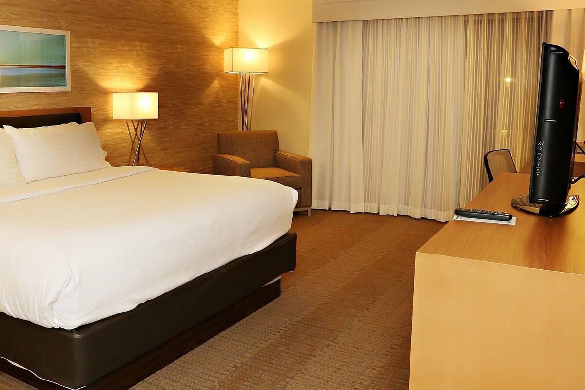 Ein Hotelzimmer mit einem großen Bett, einem Schreibtisch mit Fernseher, einem Sessel und einem Bild an der Wand.