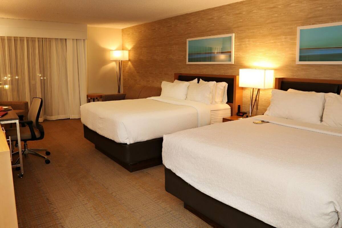 Ein Hotelzimmer mit zwei Betten, einem Schreibtisch und einem Stuhl. Zwei Wandlampen und ein Gemälde befinden sich über den Betten.