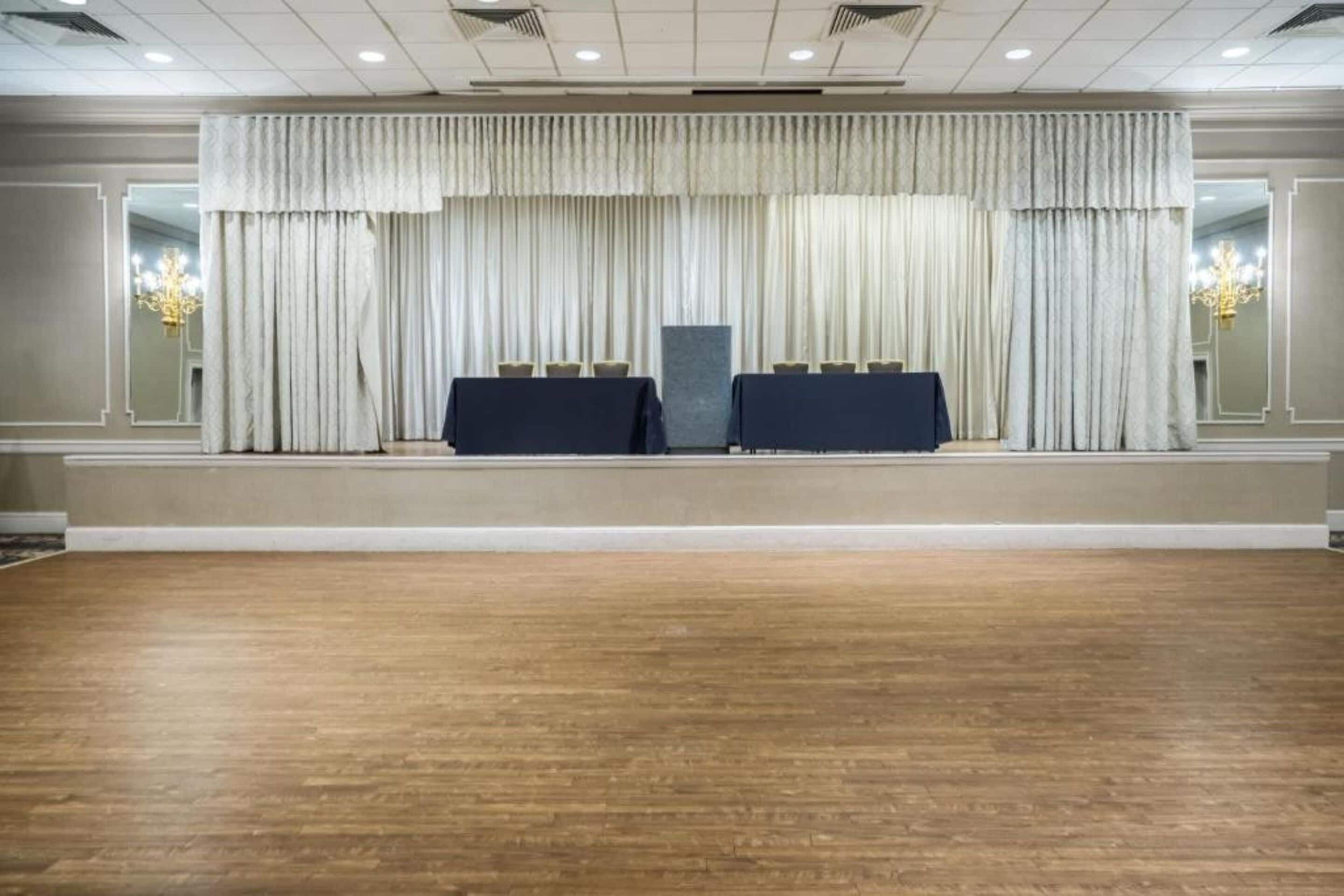 A conference room with a wooden floor, two tables with dark covers, and a large curtain backdrop.