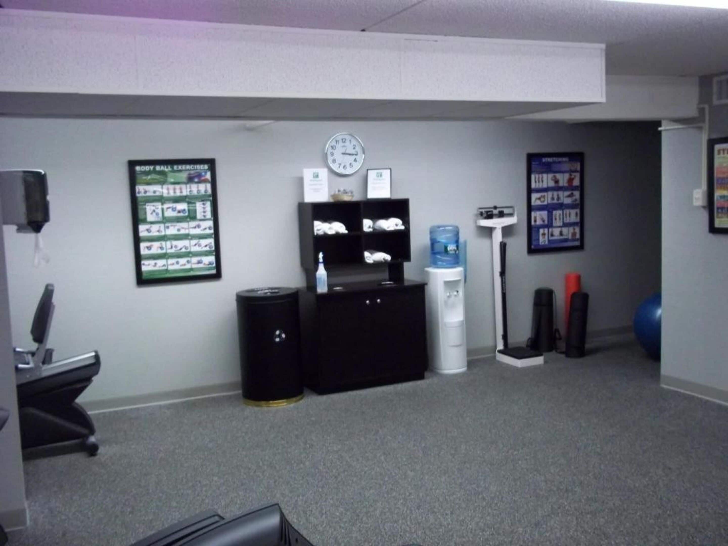 A small office with a desk, chair, water dispenser, clock, and exercise posters on the wall.