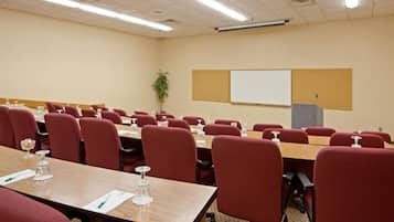 A conference room with multiple tables and red chairs, equipped with water glasses and notepads.