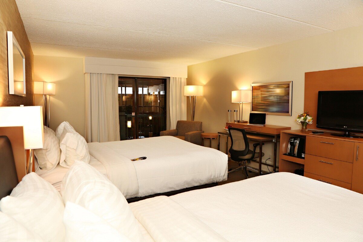 A hotel room with two beds, a desk, a chair, a TV, and a window with curtains.