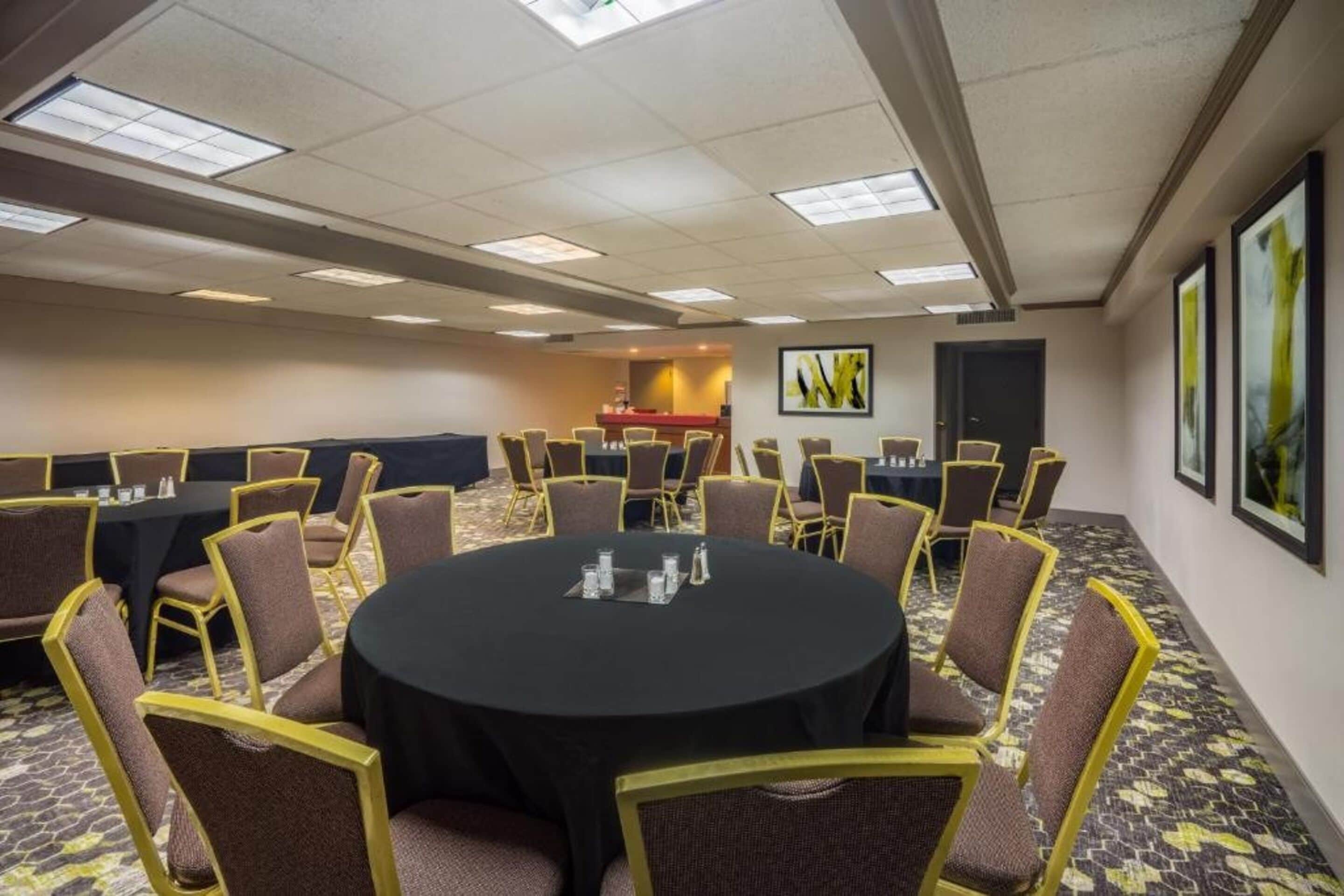 A conference room with a round table, multiple chairs, and a carpeted floor.
