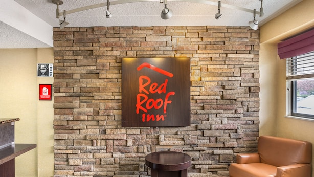 Un hall d’entrée de Red Roof Inn avec un mur en pierre, un comptoir d’accueil, une table ronde et un fauteuil en cuir.