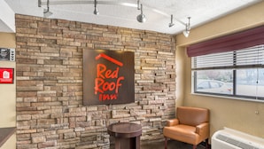 Un hall d’entrée d’un Red Roof Inn, avec un mur en pierre, un fauteuil en cuir, une petite table ronde et une grande fenêtre avec des stores.