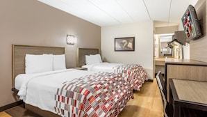 Ein Hotelzimmer mit zwei Betten, einem Schreibtisch, einem Fernseher und einem gerahmten Bild an der Wand.