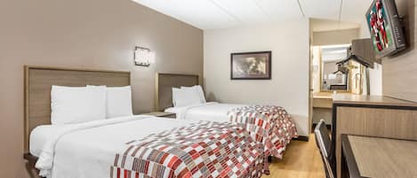 A hotel room with two beds, a desk, a television, and a framed picture on the wall.
