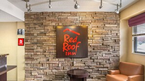 A Red Roof Inn lobby with a stone wall, a reception desk, a leather chair, and a small table. - Red Roof Inn Tinton Falls - Jersey Shore (Tinton Falls)