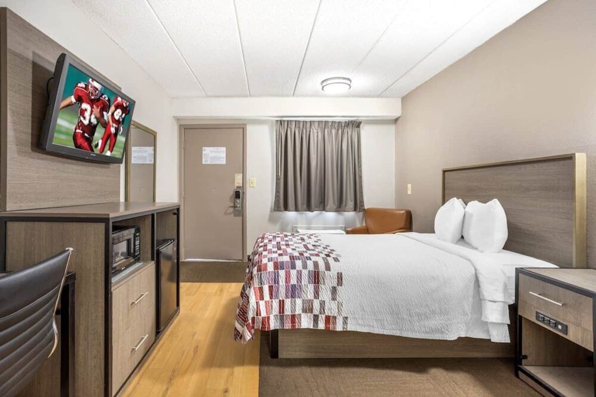 Une chambre d’hôtel avec un lit, un téléviseur fixé au mur, un bureau avec une chaise et une fenêtre avec des rideaux.