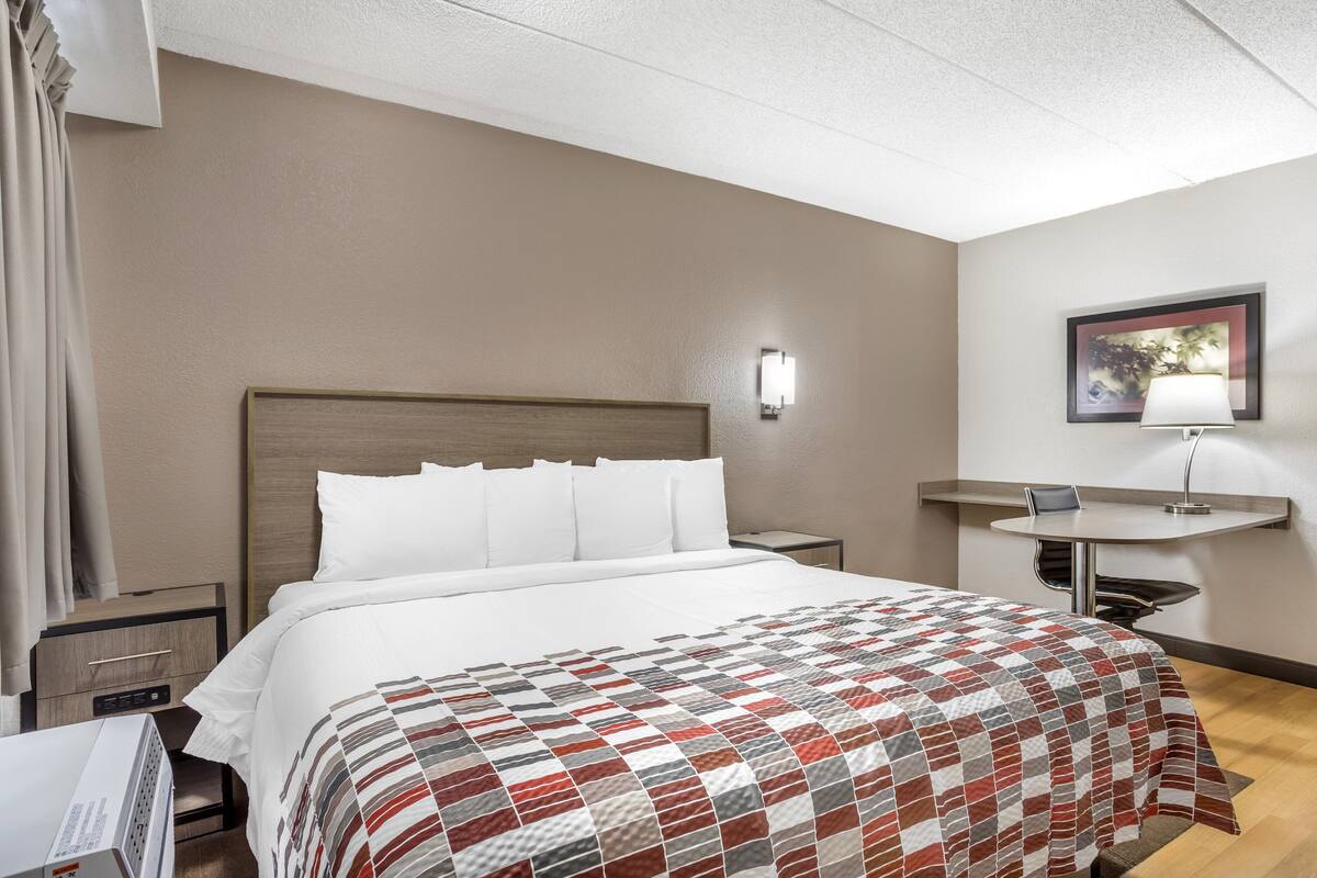 Una habitación de hotel con cama, mesita de noche, lámpara y un cuadro en la pared.