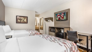 Une chambre d’hôtel avec deux lits, un bureau, une chaise, une télévision et un tableau encadré au mur.