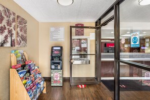 Un hall d’hôtel intérieur comprenant un comptoir d’accueil, un distributeur automatique de billets et un panneau mural affichant les règles et les politiques de l’établissement.