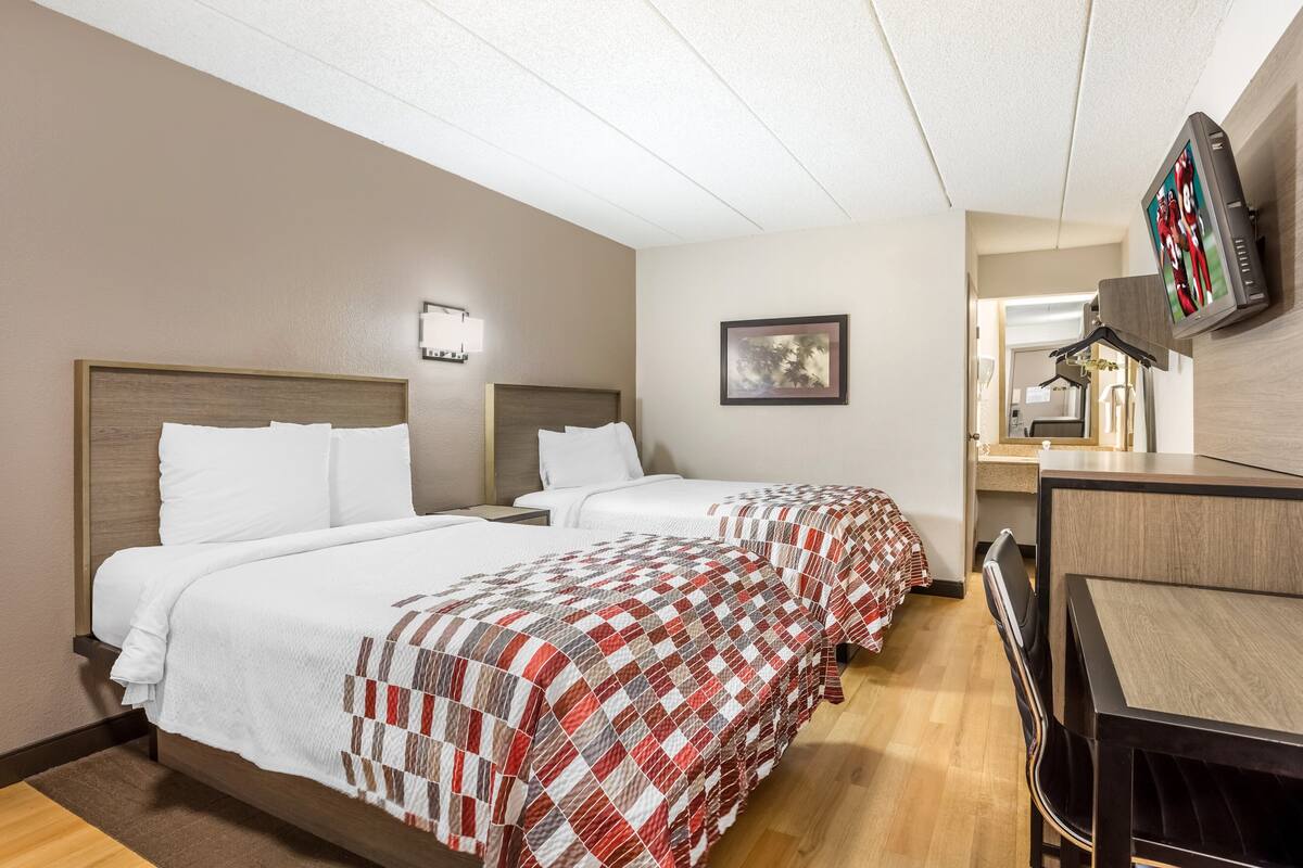 Habitación de hotel con dos camas, un escritorio, una silla, un televisor y un cuadro en la pared.
