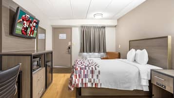 Habitación de hotel con cama, escritorio, televisión, puerta y ventana con cortinas.