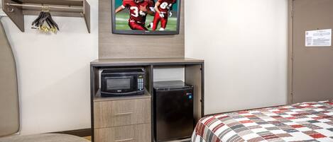 A hotel room with a bed, a microwave, a refrigerator, a TV mounted on the wall, and a small wooden cabinet.
