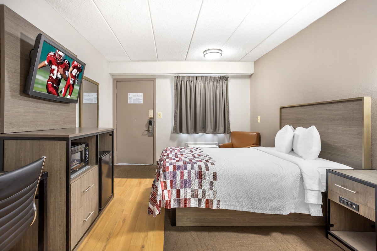 A hotel room with a bed, a TV mounted on the wall, a desk with a microwave, and a chair.