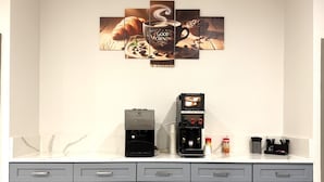 A kitchenette with two coffee makers, a coffee cup, and a croissant on the counter.