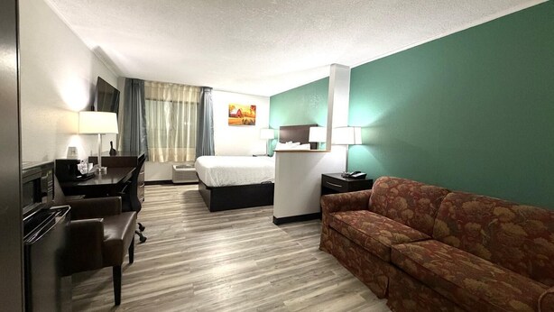A hotel room with a bed, a sofa, a desk with a lamp, a chair, and a TV.
