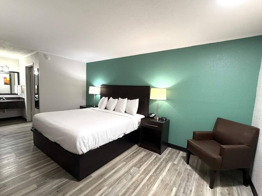 Une chambre d’hôtel comprenant un lit, une table de chevet, une lampe, une chaise et une salle de bain avec un miroir et un lavabo.