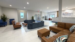 A modern hotel lobby with seating areas, a reception desk, and a large window with the word 'OPEN' visible.