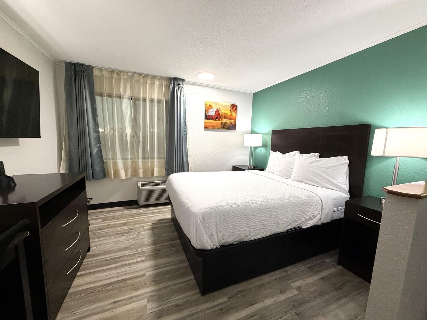 A hotel room with a bed, bedside tables, a desk, a chair, a TV, and a window with curtains.