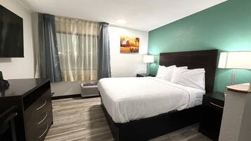 A hotel room with a bed, bedside tables, a desk, a chair, a TV, and a window with curtains.