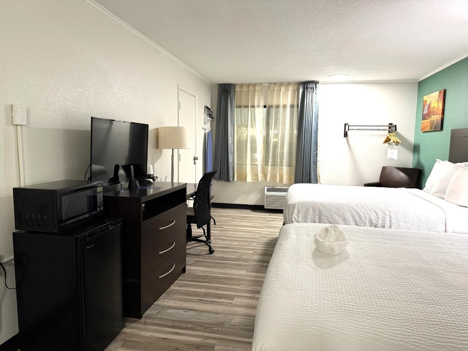 Een hotelkamer met een bureau, een televisie, een bed en een raam met gordijnen.