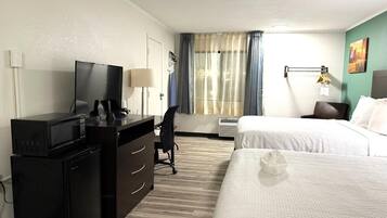 Een hotelkamer met een bureau, een televisie, een bed en een raam met gordijnen.