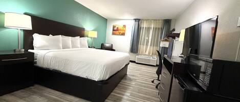 A hotel room with a bed, bedside tables, a desk with a chair, a television, and a window with curtains.