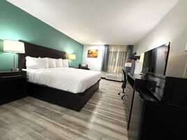 Habitación de hotel con cama, mesitas de noche, escritorio con silla, televisión y ventana con cortinas.