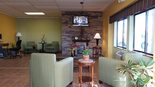 Un hall con sillones verdes, chimenea, televisor y un ventanal grande.