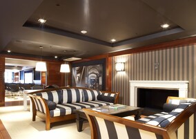 A modern lounge area with striped sofas, a fireplace, and a dining area in the background.
