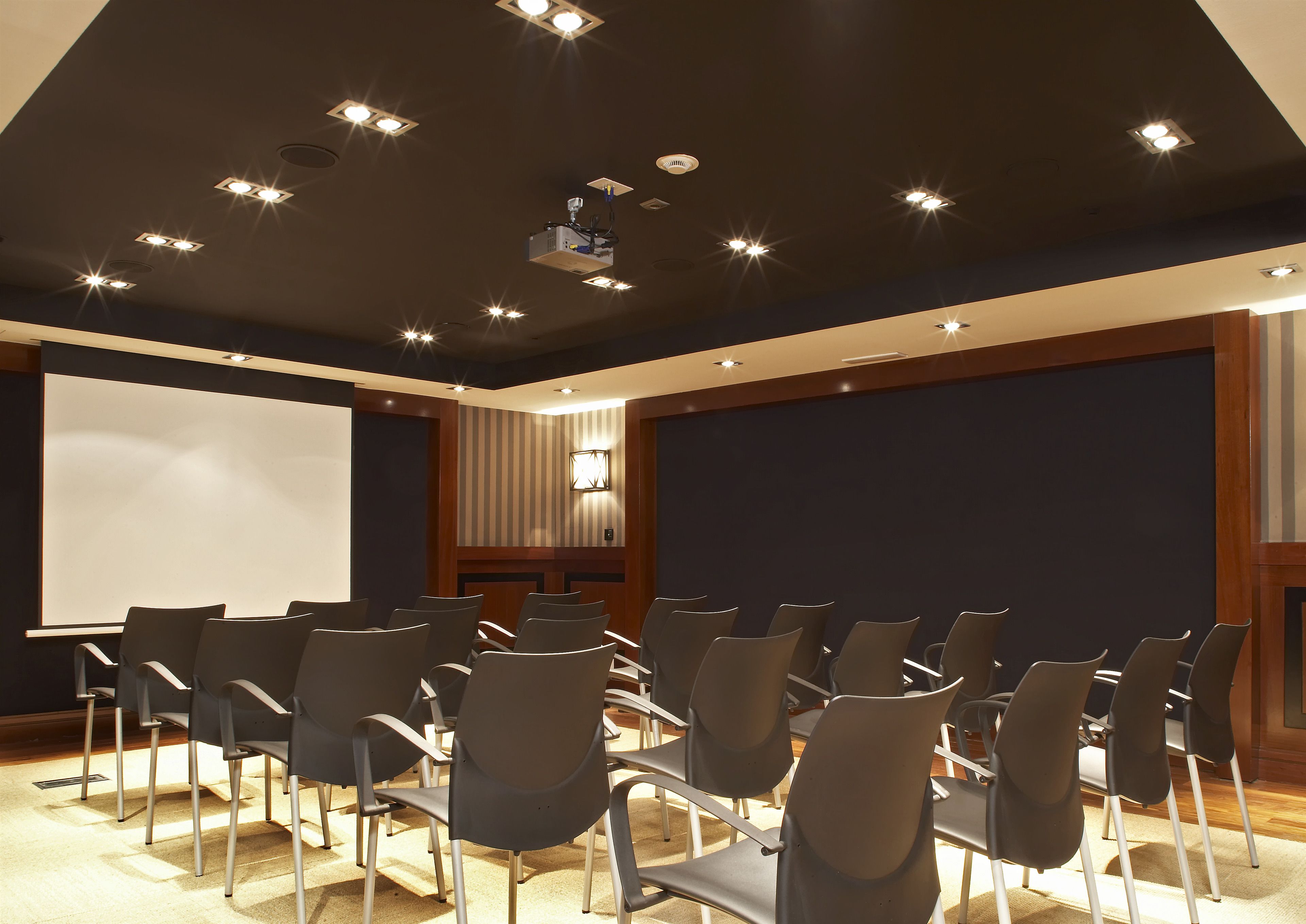 Un salón de conferencias con hileras de sillas, un proyector y una pantalla grande.