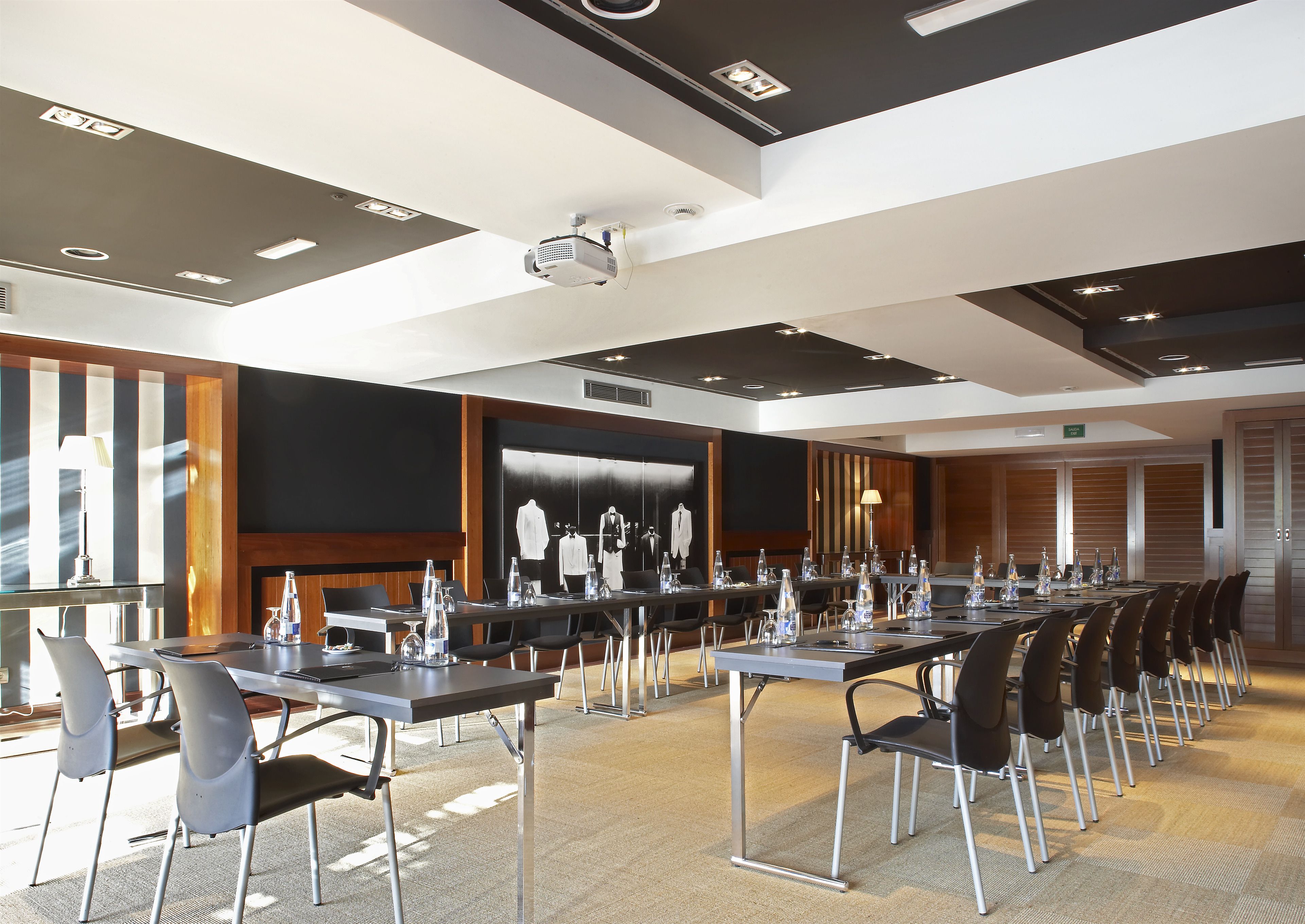 Une salle de conférence équipée de longues tables, de chaises, d’un projecteur et d’un grand écran.