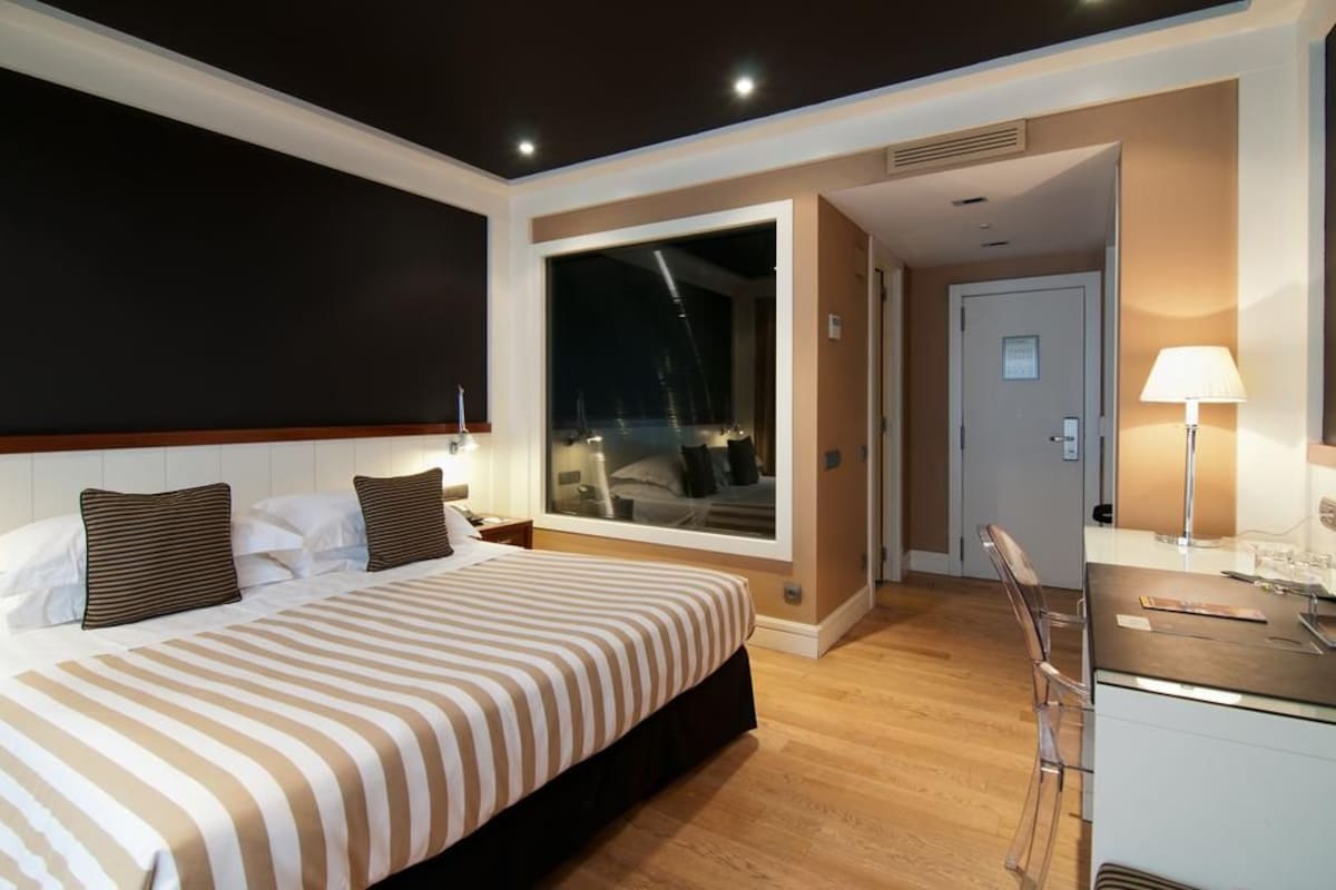 Habitación de hotel con una cama grande, un escritorio con una silla y una ventana que ofrece vista a la ciudad de noche.