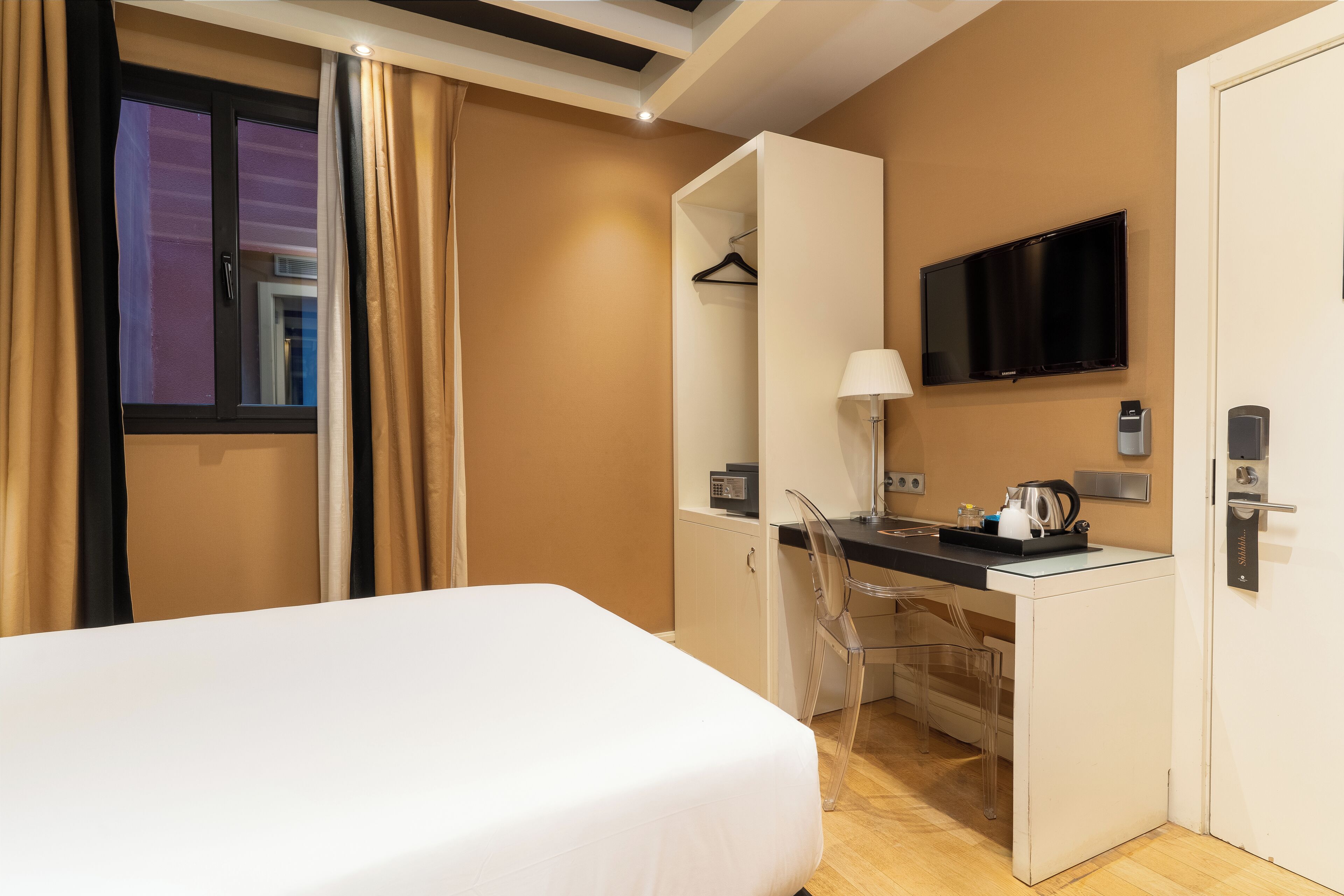 Una habitación de hotel con cama, escritorio, silla, televisor y armario.