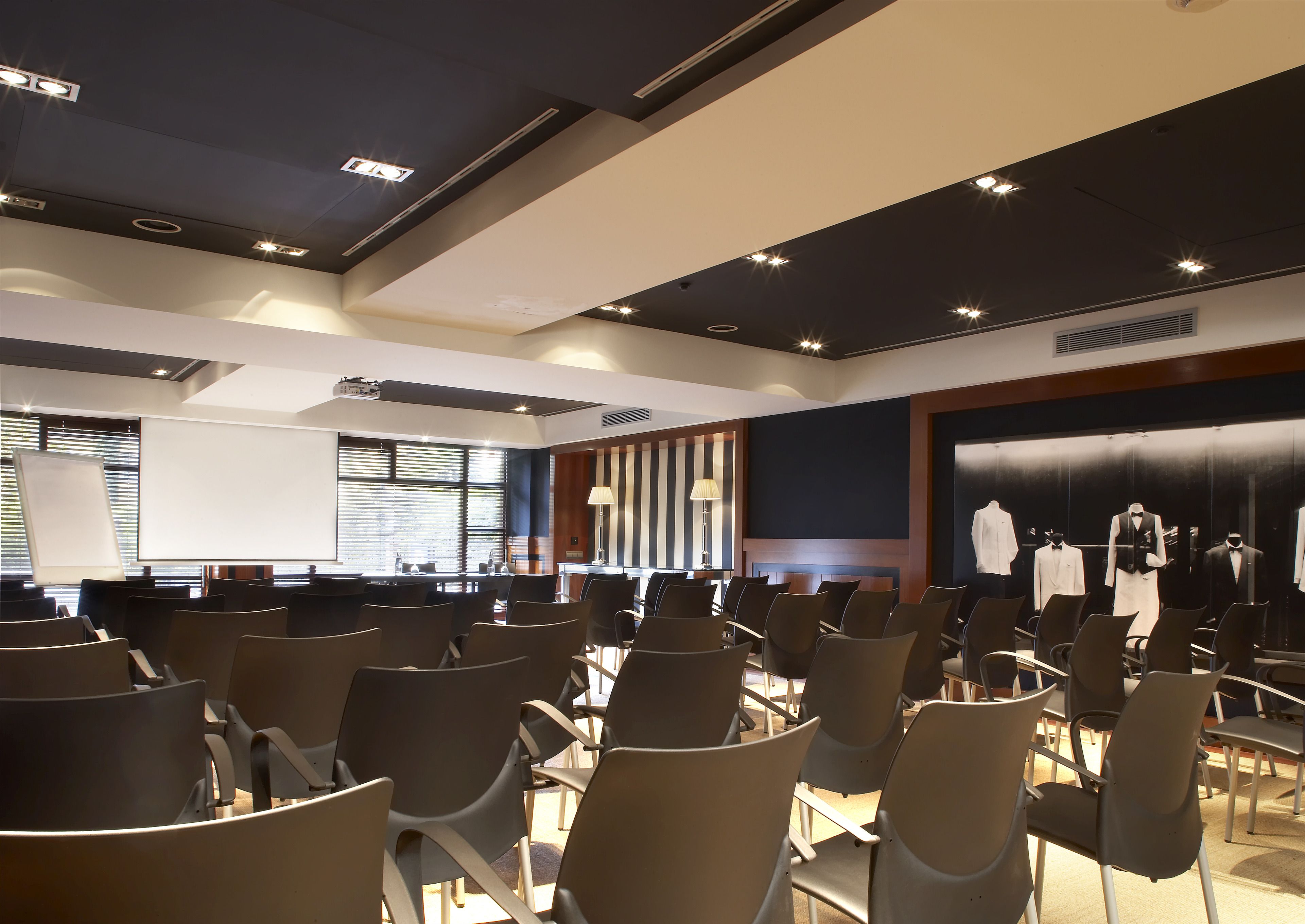 A conference room with rows of chairs, a projector screen, and a display of formal wear.