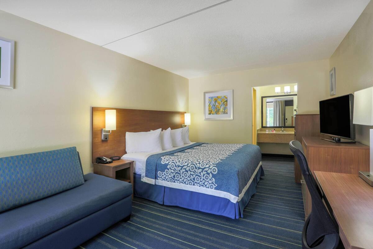 Een hotelkamer met een bed, een slaapbank, een bureau, een televisie en een badkamer zichtbaar door een open deur.